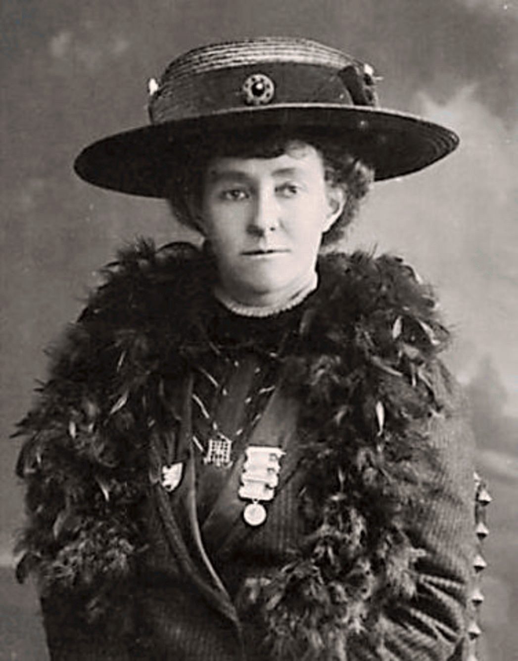 A black and white portrait of a woman in a wide-brimmed hat and feathery scarf.