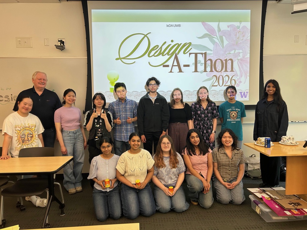 A group of students standing in a classroom in front of a screen displaying a design-a-thon logo.