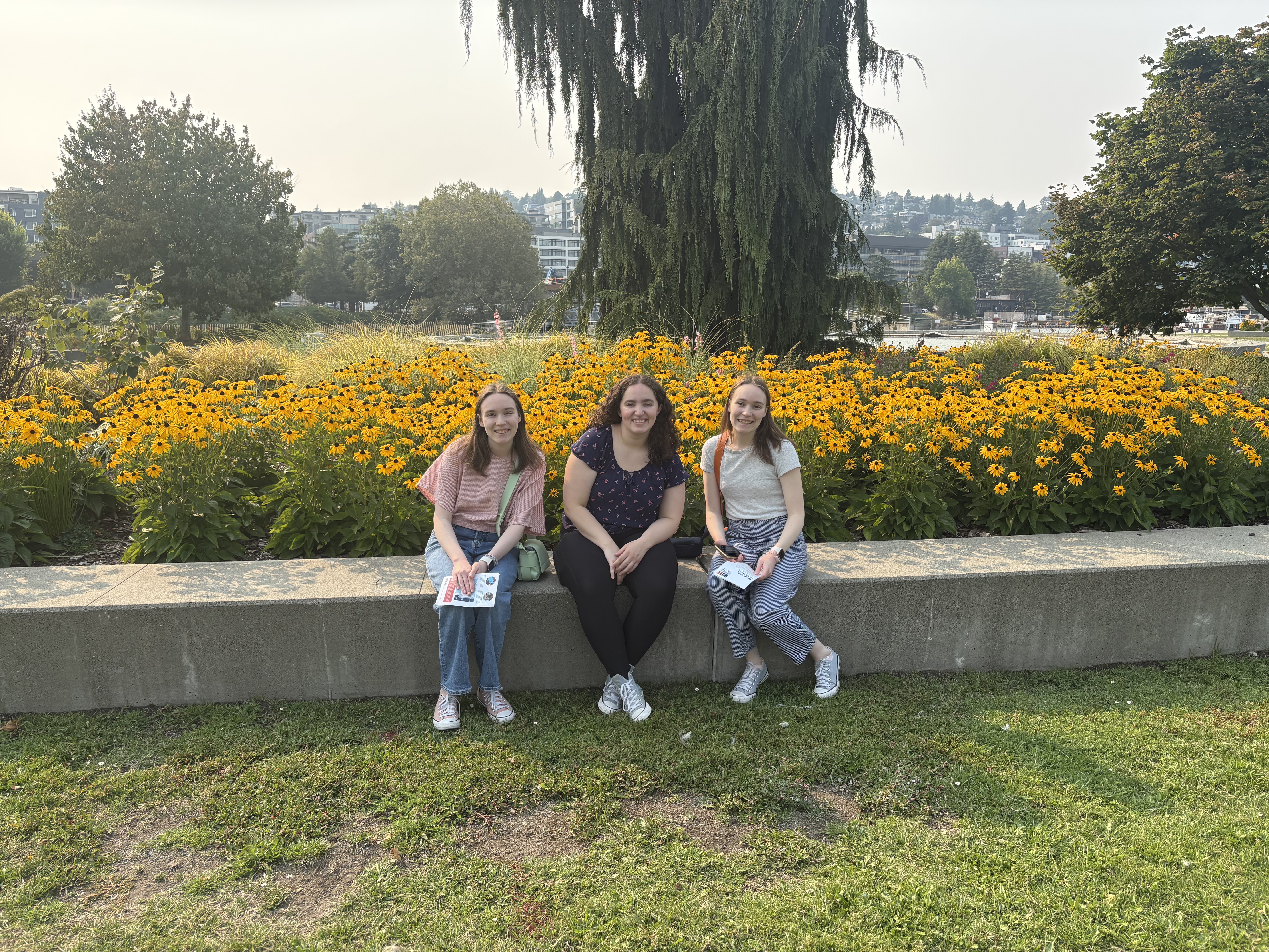 Three girls sitting in front of yellow flowers.