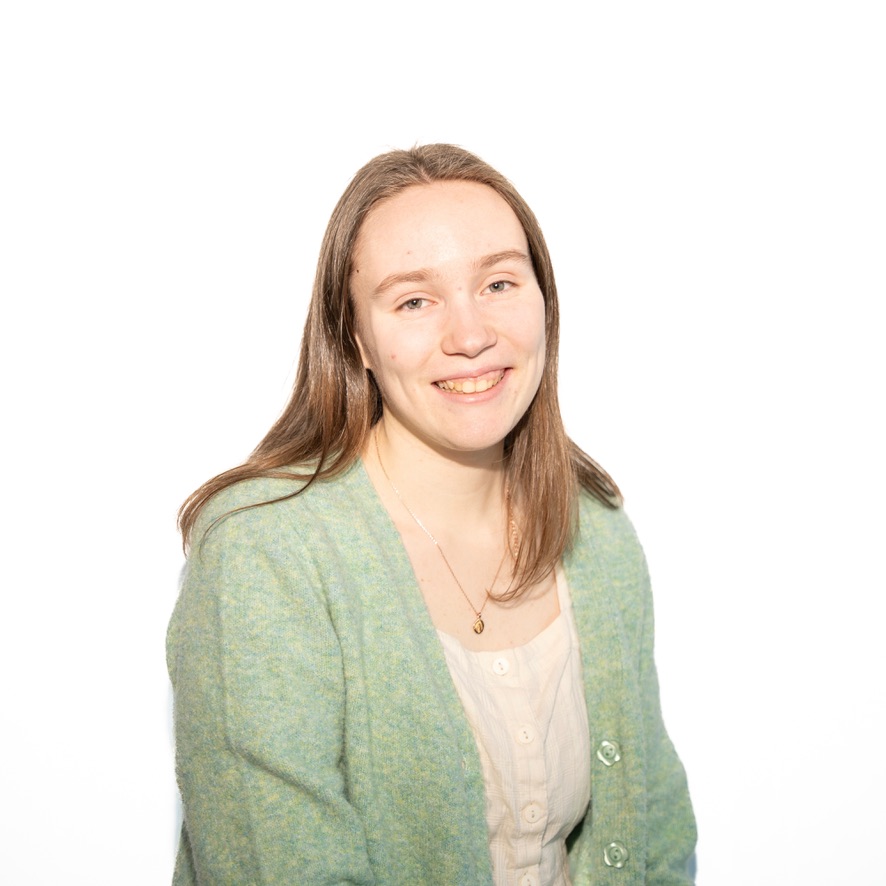 A headshot of a girl in a green sweater and white shirt.
