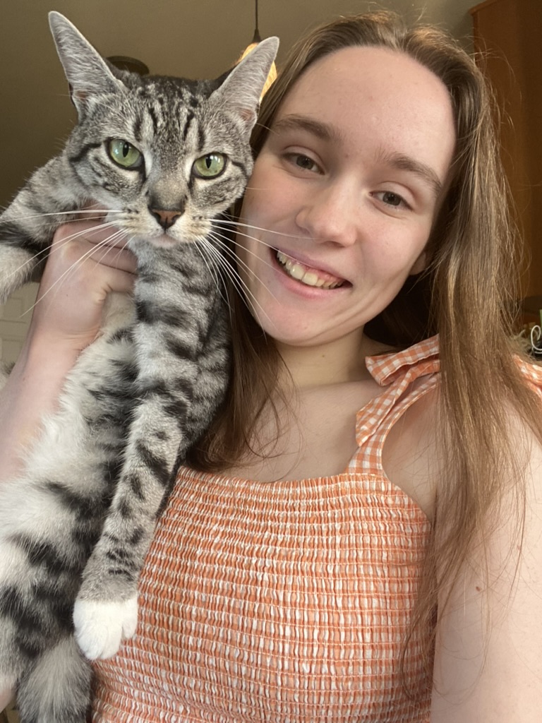 A girl dressed in orange holding a gray tabby cat.