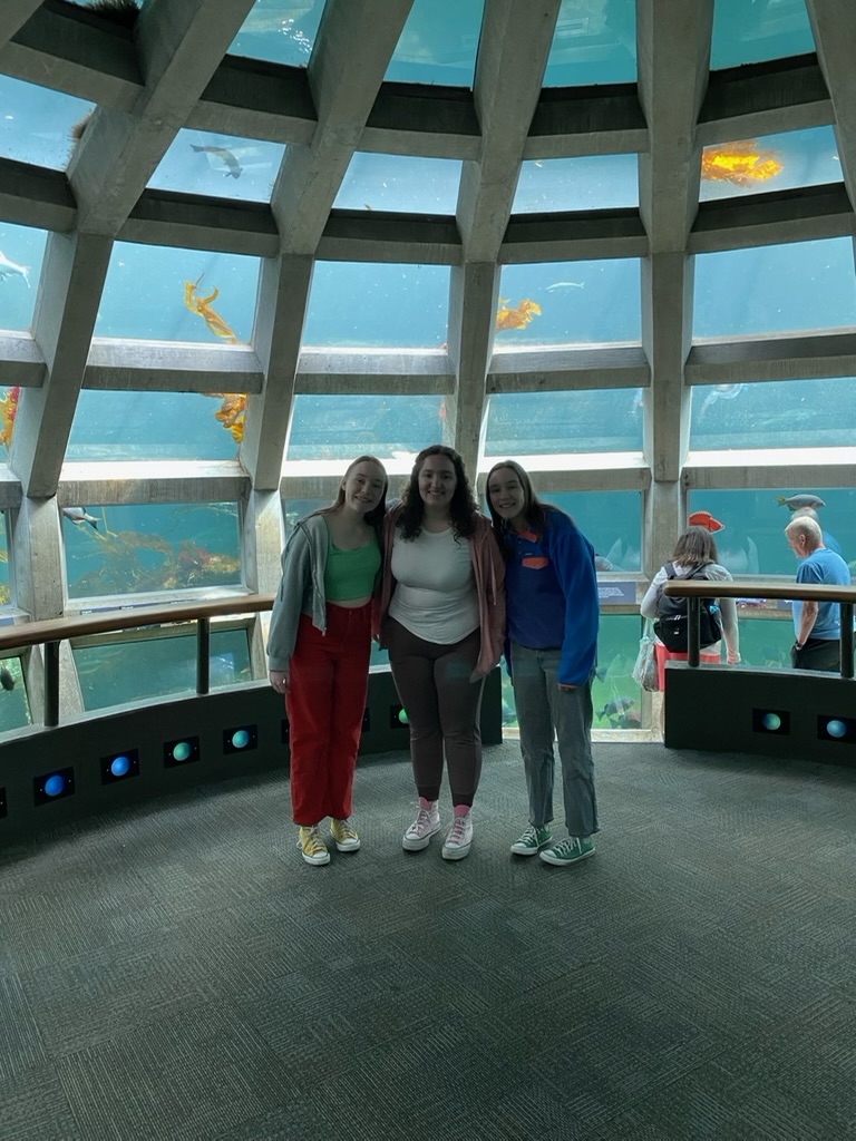 Three girls standing in front of a dome shaped floor to ceiling fish tank.