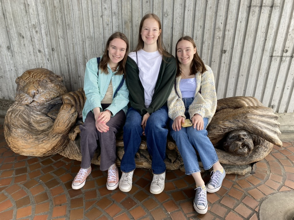 Three girls sitting on a wooden otter bench.