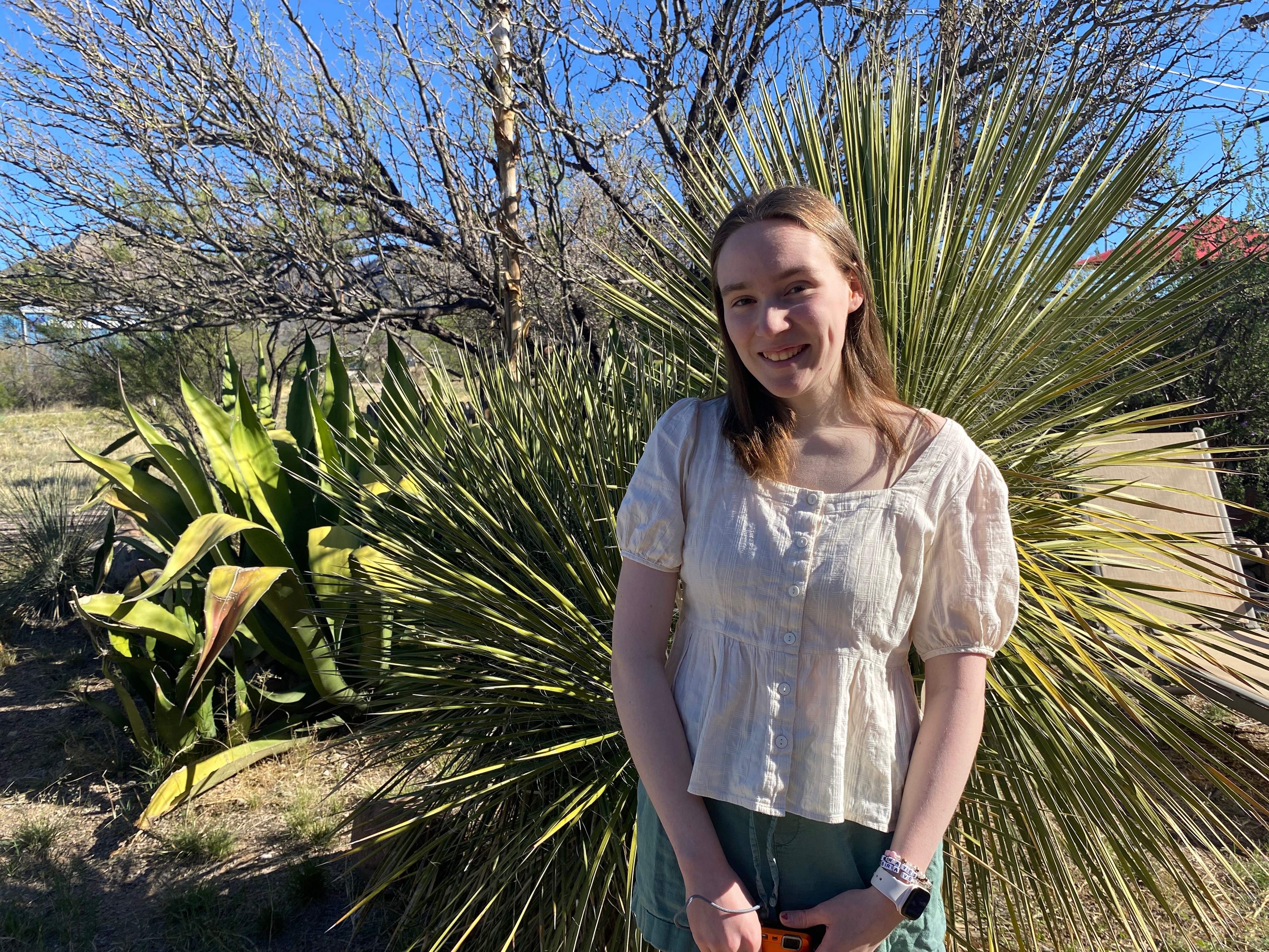 A girl standing in front of desert plants on a sunny day.