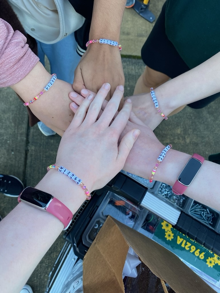 Five hands piled up together with beaded bracelets.