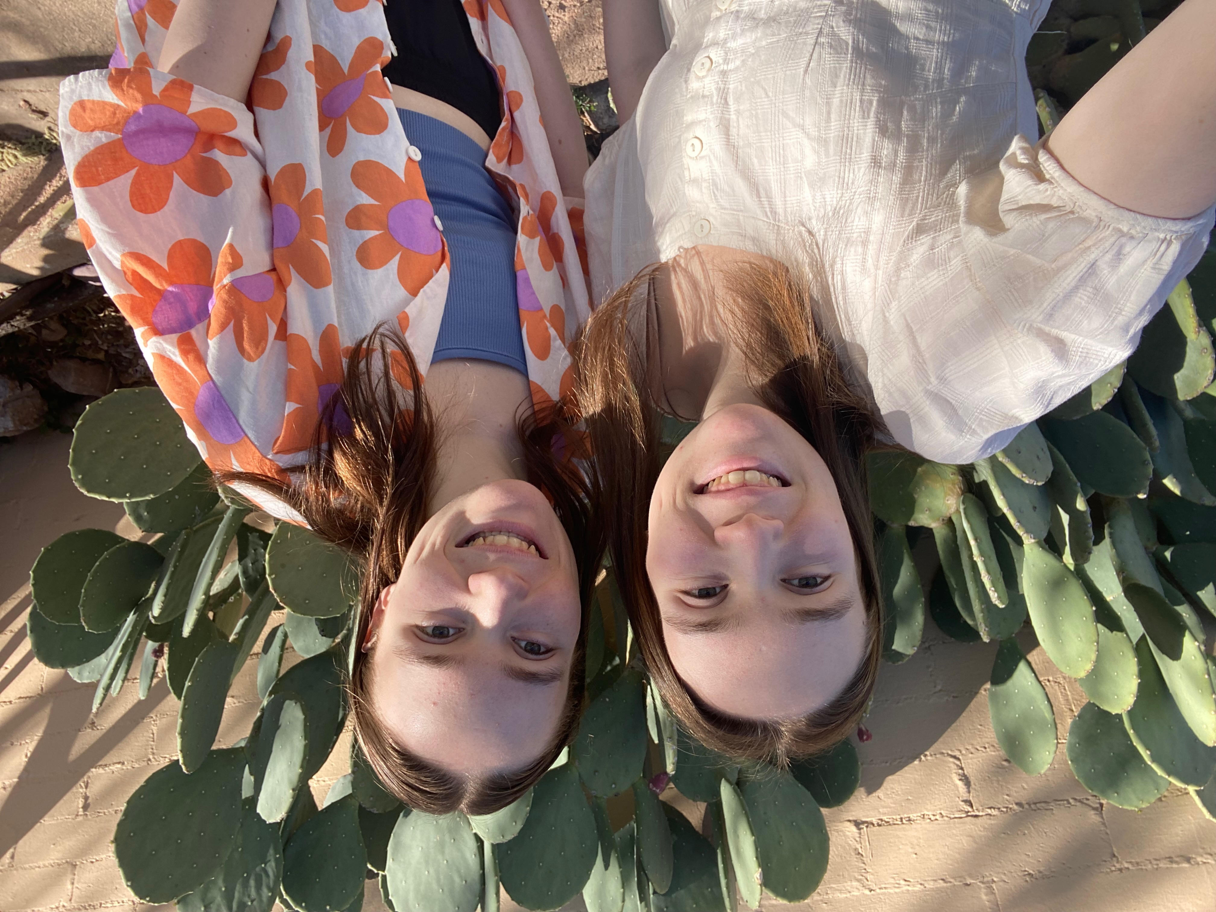 Two girls standing in front of a cactus on a sunny day.