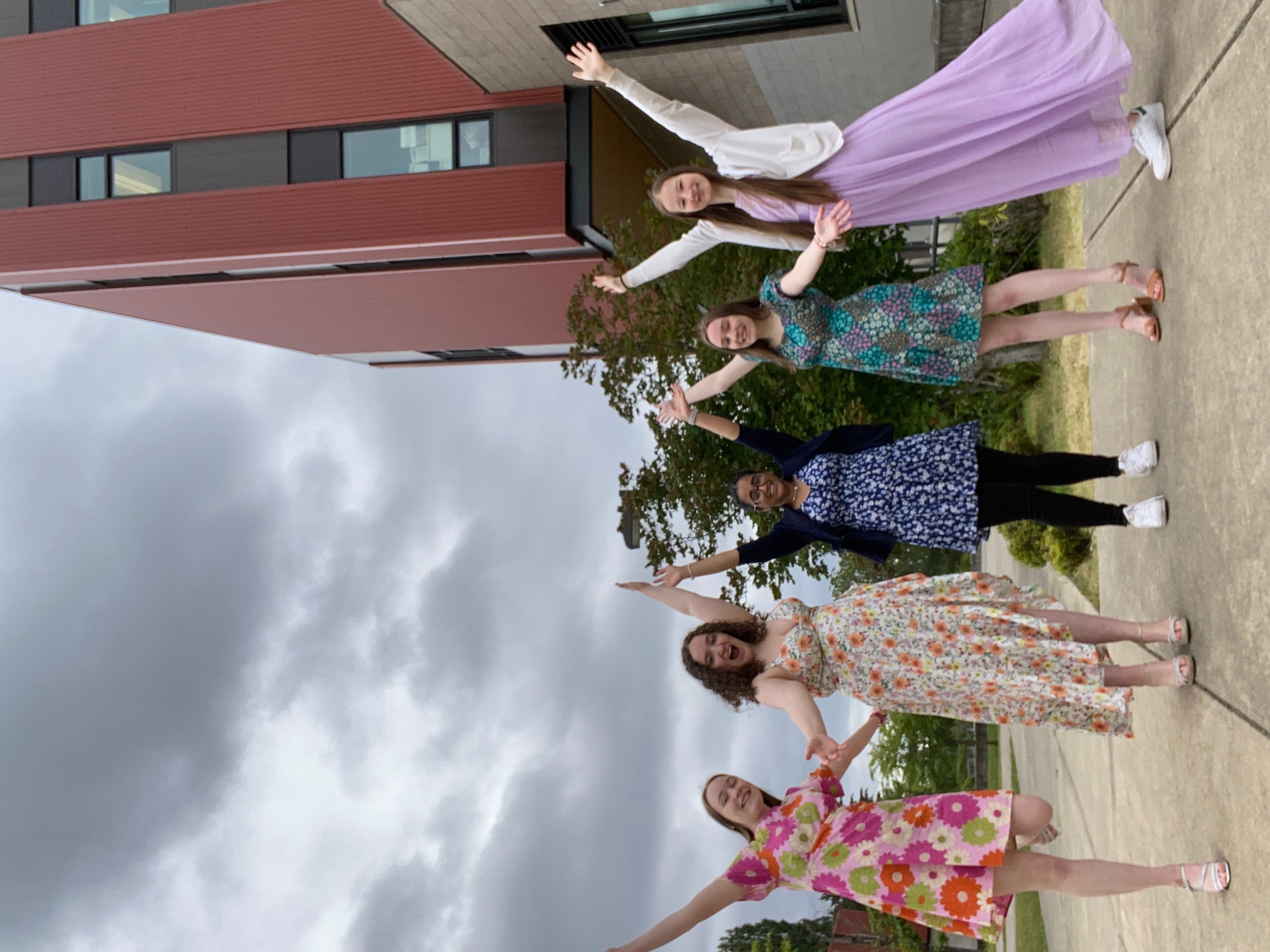 Five girls in dresses with their hands in the air.