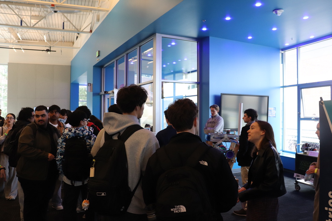 A crowd of people standing around a rover talking.