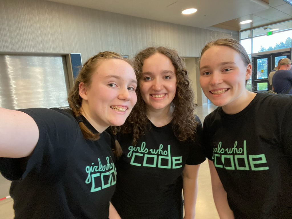 Three girls smiling wearing Girls Who Code shirts.