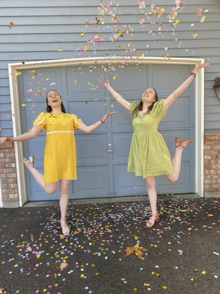 Two girls in dresses throwing confetti in the air in front of a blue wall.