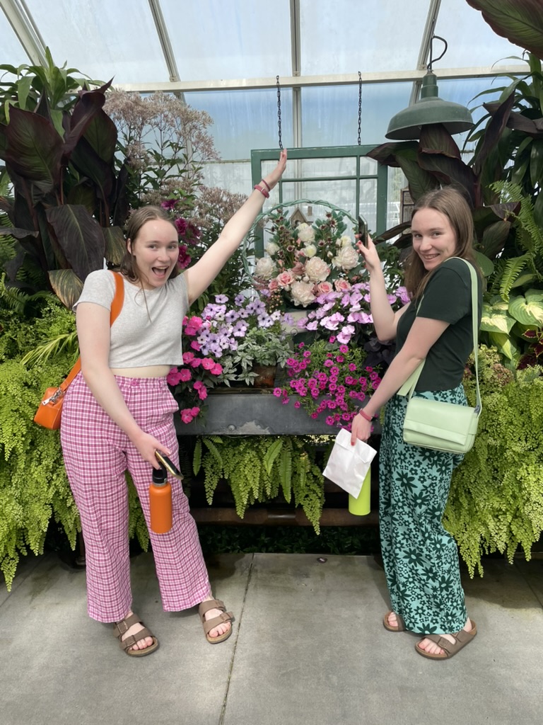Two girls besides colorful flowers in a greenhouse.