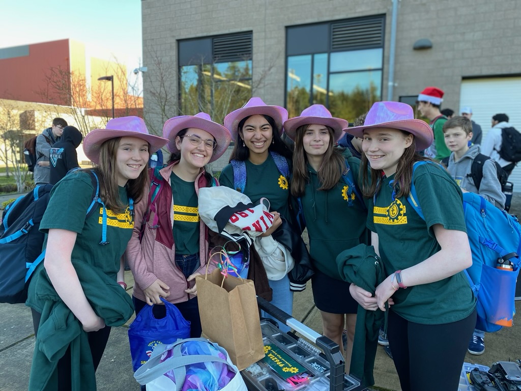 Five girls in pink cowboy hats standing outside next to a pile of bags and toolboxes.