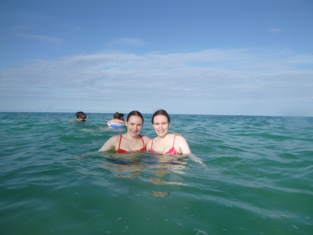 Two girls swimming in the ocean with a cloudy blue sky.