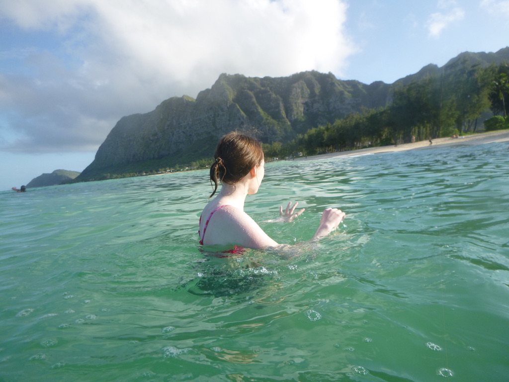 A girl swimming in the ocean in front of a mountain.