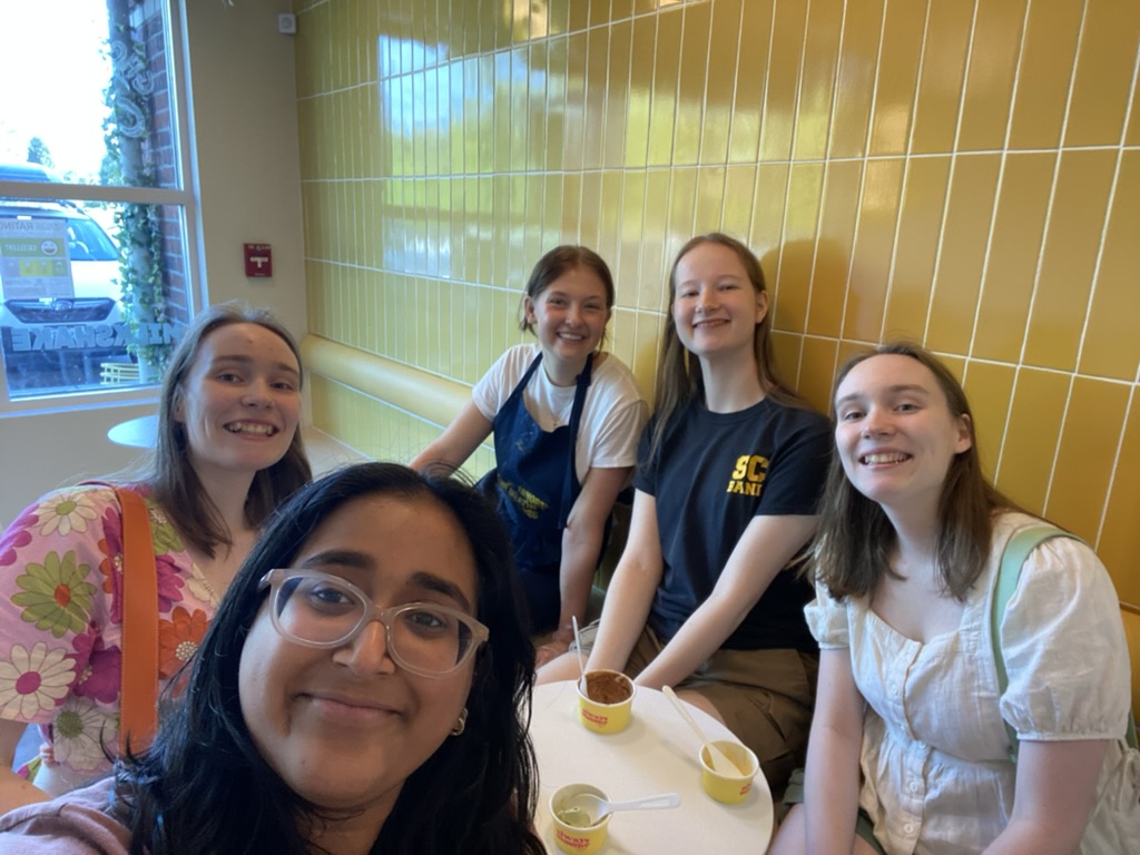 Five girls sitting at a table eating ice cream in front of a yellow tiled wall.
