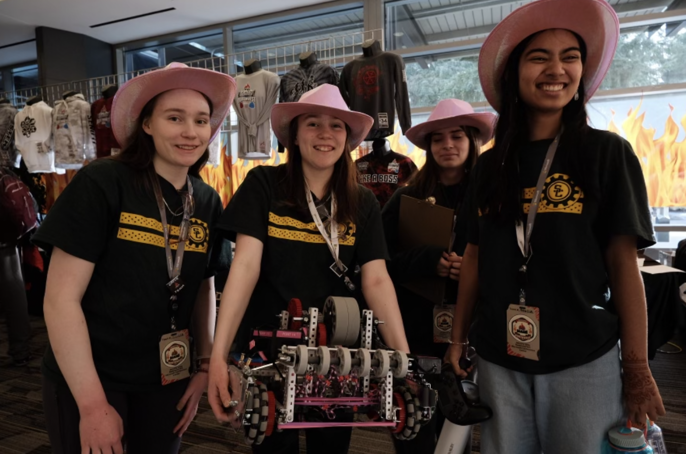 Four girls in pink cowboy hats holding a robot standing in a hallway.