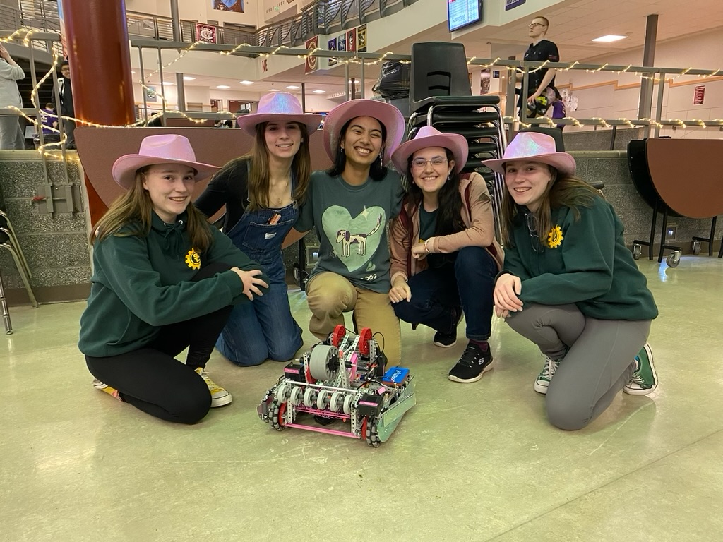 Five girls in pink cowboy hats crouched around a pink robot.