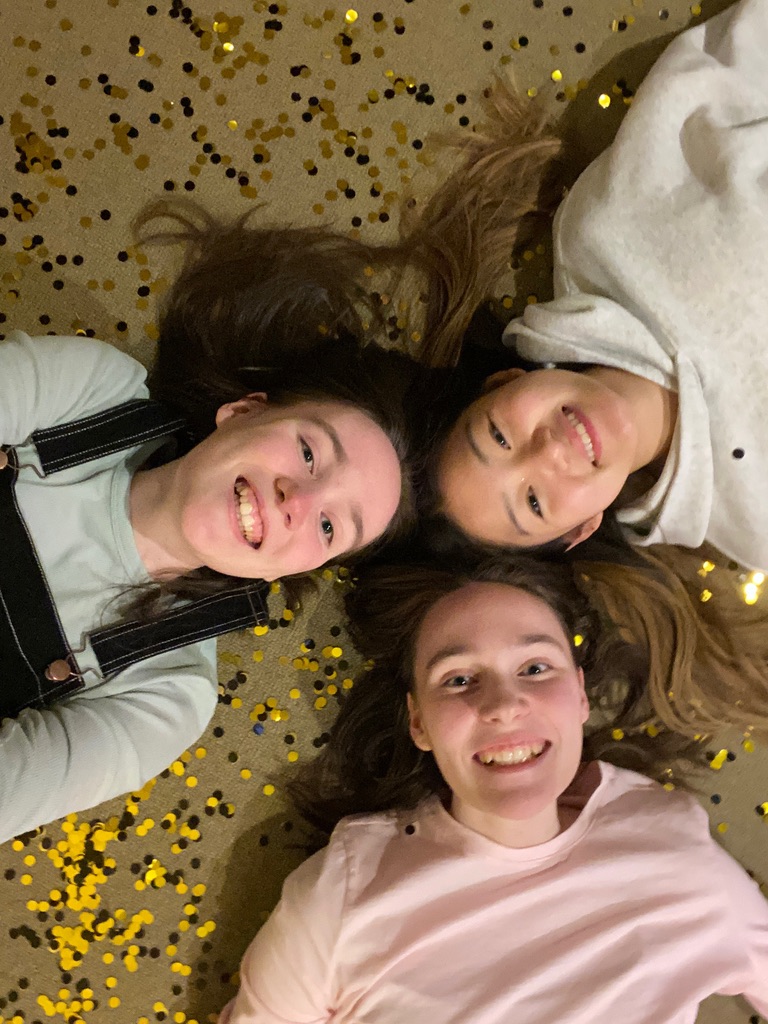 Three girls laying on the floor surrounded by confetti.