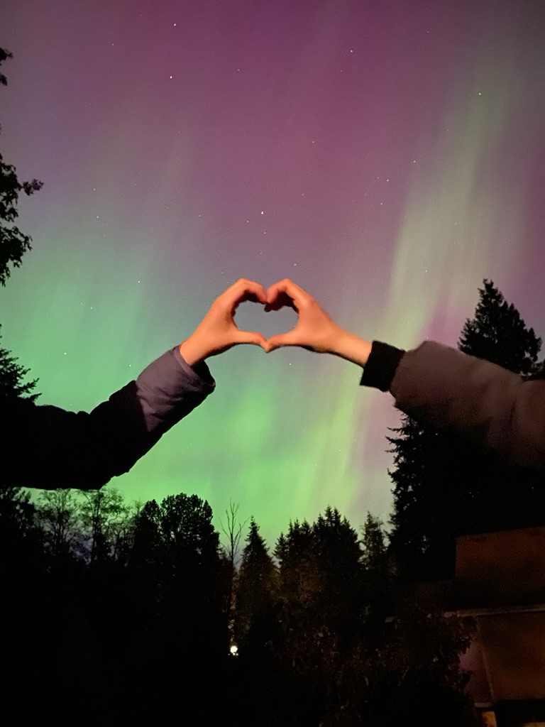 Two hands making a heart shape in front of the northern lights.