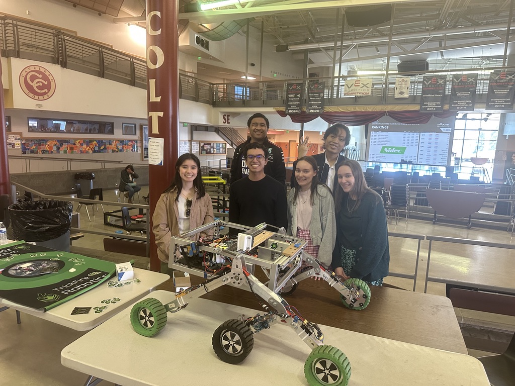 Three girls and three guys standing beside a table with a rover.