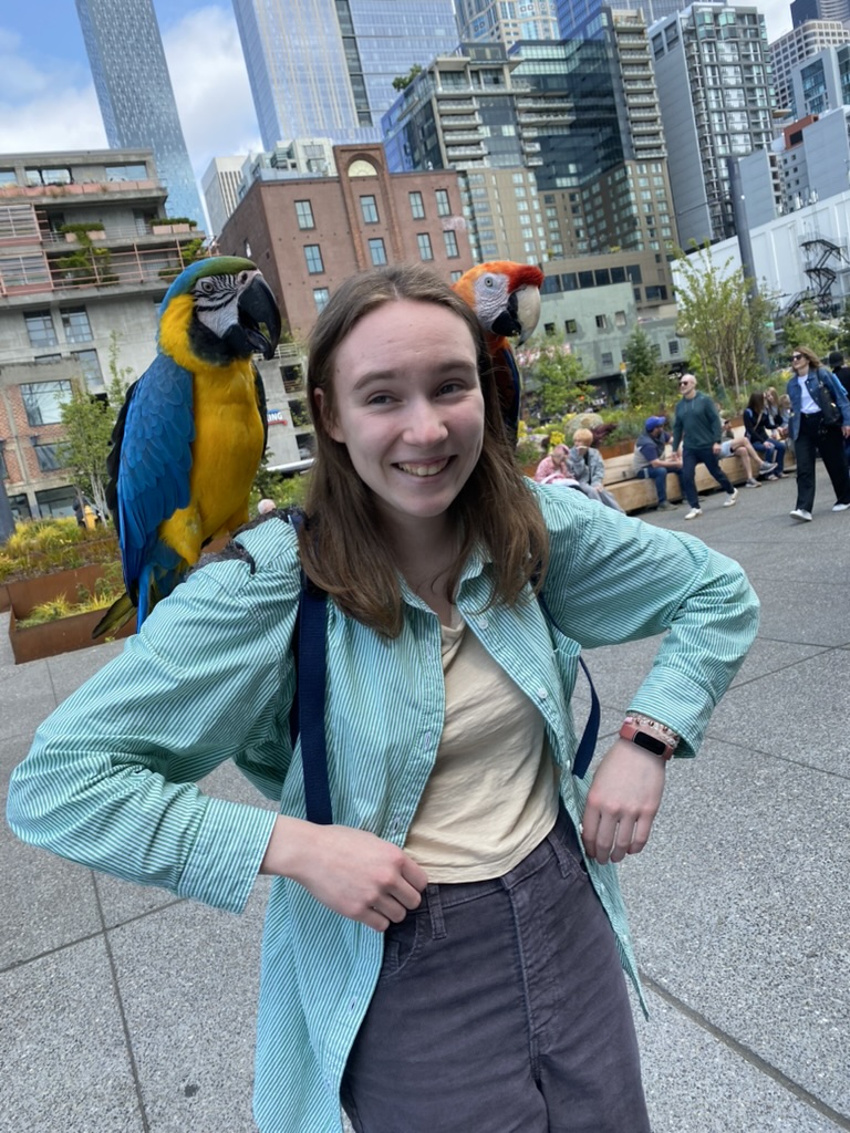 A girl with two colorful birds on her shoulders.