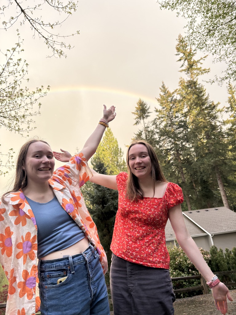 Two girls with their arms in the air in front of a rainbow.