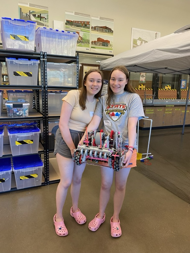 Two twins holding up a pink robot in a classroom.