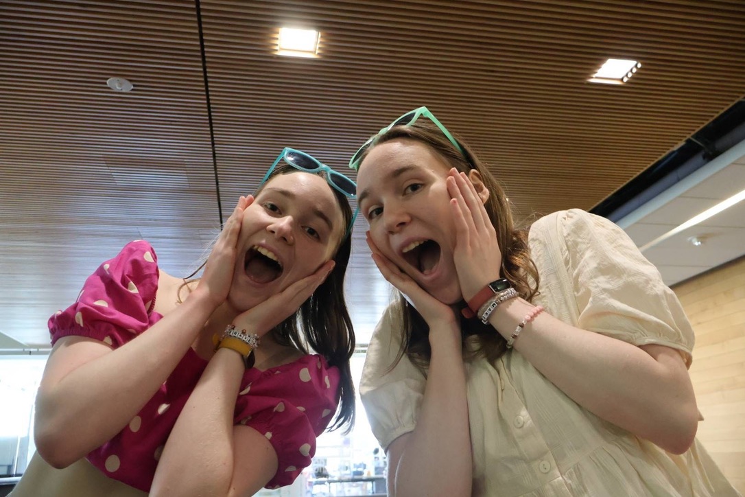 Two girls wearing sunglasses putting their hands on their cheeks.