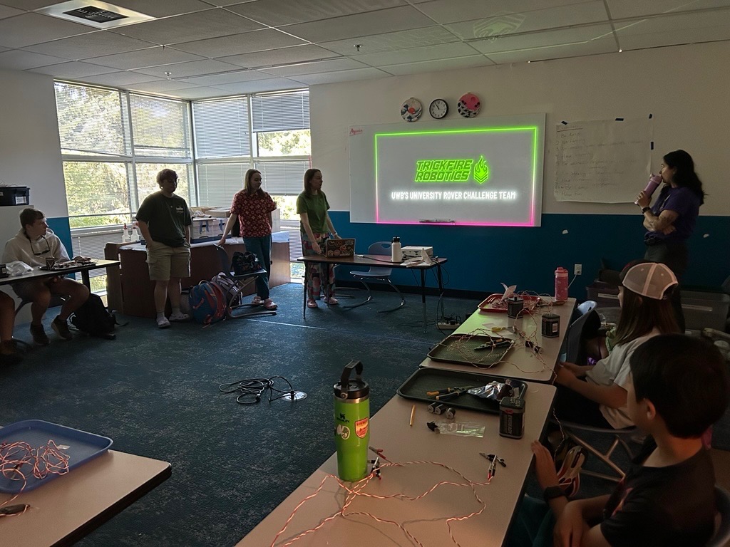 Three students presenting in front of a group of kids.