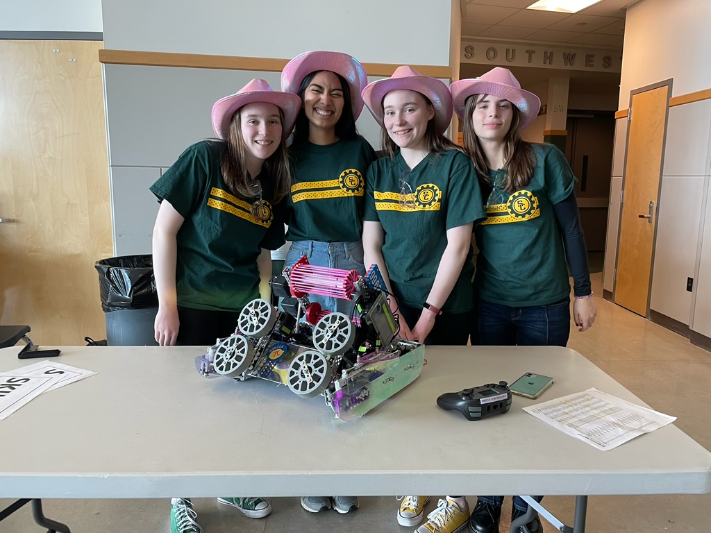 Four girls in pink cowboy hats standing around a table with a pink and purple robot on it.